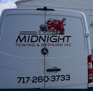 The back of a Midnight Towing and Repairs service van showing the company phone number